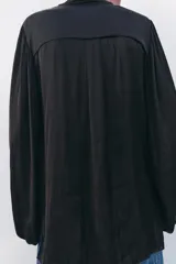 Camisa fluida negra de cuello redondo con lazada, manga larga tipo globo con pliegues en hombro y cierre frontal con botones ocultos por solapa.