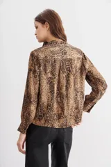 Camisa fluida con estampado reptil, escote redondo con apertura frontal y mangas largas terminadas en puño con botón.