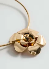 Gargantilla rígida dorada con aplique de flor metálica.