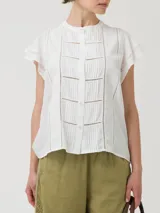 Blusa blanca de lino orgánico y viscosa, con cuello redondo, cierre frontal con botones, mangas cortas con volados y broderie con calados en el frente.
