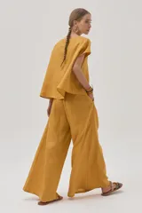 Pantalón de lino color mostaza, de corte palazzo, con lazo en la cintura, pinzas en el frente y bolsillos laterales.