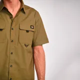 Camisa de manga corta color verde oliva con dos bolsillos de parche en el pecho con cierre de solapa y botón. Logo de Caterpillar bordado en la solapa del bolsillo izquierdo. Corte recto y cierre frontal con botones.