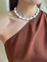 Collar corto de cuentas blancas de diferentes formas y tamaños, unidas por un hilo transparente.