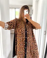 Camisola corta con estampado de leopardo, cuello camisero, cierre frontal con botones y mangas cortas con puños. Presenta paneles laterales negros.