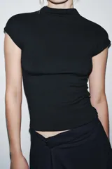 Top sin mangas, color marrón topo, con cuello alto y corte recto. Presenta un tejido de punto fino y mangas sisa con caída.