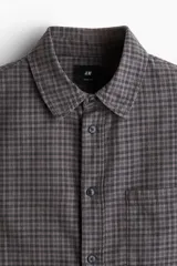 Camisa de franela suave a cuadros grises y marrones, de corte holgado, con cuello inglés, tapeta clásica, canesú en la espalda, bolsillo superior abierto, mangas largas con tapeta de manga y puños abotonados, y bajo levemente redondeado.