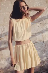 Top cropped color crema, sin mangas, de punto suave con costuras fruncidas para una silueta abullonada con efecto drapeado.