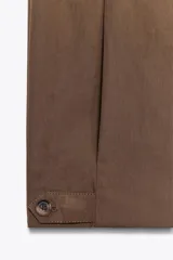 Pantalón marrón de tiro medio con trabillas en la cintura, bolsillos laterales, pinzas delanteras y bajo ajustable con trabilla y botón.