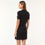 Vestido corto negro de punto grueso con botones dorados al frente, cuello redondo y mangas cortas. Presenta bolsillos de parche a la altura del busto y en la falda.