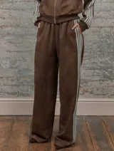 Conjunto deportivo marrón de dos piezas: campera con cremallera, cuello alto, mangas largas con puño y detalles de rayas blancas en mangas y laterales del pantalón. Pantalón recto de cintura alta con cordón ajustable.