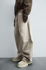 Pantalón de jean color beige, de corte amplio y tiro alto, con cinco bolsillos, efecto lavado y cierre frontal con botones.