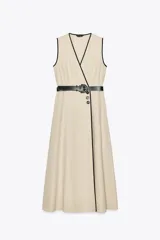 Vestido midi de lino color beige, con escote cruzado en pico y sin mangas. Presenta vivos a contraste en negro y cinturón con hebilla forrada. Cierre frontal con botones.