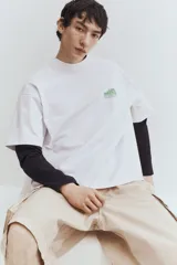 Remera blanca de algodón pesado con cuello redondo y estampado pequeño en el pecho. Corte oversized con hombros caídos y bajo recto.