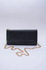 Cartera tipo sobre color negro con textura granulada, cierre con solapa y múltiples ranuras interiores. Incluye bolsillo interior con cierre para monedas y cadena metálica dorada regulable para usar al hombro o como bandolera. Forro textil rojo.