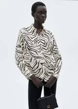 Camisa de manga larga con estampado animal print de cebra en blanco y negro, con cuello camisero y cierre frontal con botones.