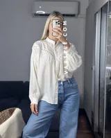 Camisa blanca de mangas largas con detalles de encaje en el cuello y en el frente.