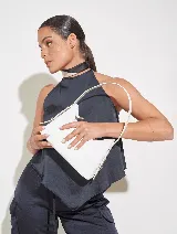 Cartera de mano color blanco con efecto charol, asa corta y cierre superior.