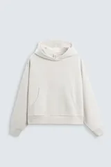 Sudadera con capucha color crudo, corte boxy, manga larga y bolsillo tipo canguro.
