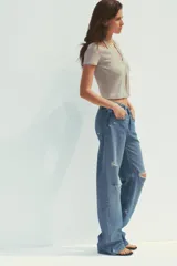 Camiseta color beige de tejido de punto, con cuello halter y escote pico. Tiene cierre frontal con botones y mangas cortas.
