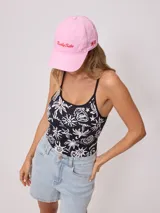 Gorra de visera color rosa claro, estilo dad hat, confeccionada en lona de algodón. Presenta bordado frontal con el texto "Rusty Tribe" en rojo y un pequeño diseño floral rojo en el lateral.