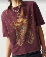 Remera color borgoña con estampa de corazón con ojo, sombrero de cowboy, cactus y mariposa. Corte holgado y mangas cortas.