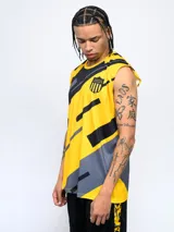 Musculosa deportiva sin mangas, color amarillo con diseño gráfico abstracto en negro y gris. Presenta un escudo de equipo de fútbol en el pecho izquierdo.