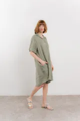 Vestido camisero corto color verde oliva, confeccionado en lino 100%. Tiene botones en la parte delantera, cuello camisero, mangas cortas con botón para arremangar y bolsillos laterales.