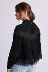 Blusa negra con cuello alto y mangas largas, con detalles de encaje en el pecho, mangas y ruedo.