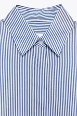 Camisa de cuello solapa y manga tres cuartos con puño ancho. Tiene aberturas laterales en el bajo y cierre frontal con botones ocultos.