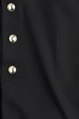 Short pollera tiro alto color negro, con elástico oculto en la cintura, pliegues y botones decorativos dorados en el frente.