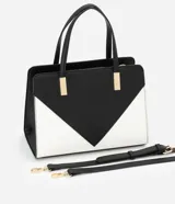 Bolso satchel mediano bicolor, negro en la parte superior y blanco en la inferior, con detalles metálicos dorados en las asas. Incluye correa larga desmontable y cierre de cremallera.