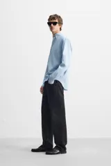 Camisa celeste de corte regular fit, confeccionada en popelín de algodón. Tiene cuello abotonado, manga larga con puños abotonados y cierre frontal con botones.