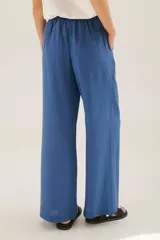 Pantalón de lino azul de corte palazzo con botón decorativo en la cintura.