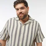 Camisa de manga corta con rayas verticales color crema y gris. Tiene cuello clásico y cierre frontal con botones.