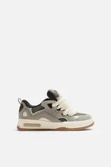 Zapatilla deportiva estilo skate color gris y verde, con cordones anchos color crema, lengüeta acolchada, tirador trasero y suela gruesa de goma color caramelo.