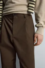 Pantalón relaxed fit color marrón confeccionado en tejido de algodón con estructura twill. Cintura con pliegues frontales, bolsillos laterales en cadera y detalle de bolsillos traseros de doble vivo con botón. Cierre frontal con cremallera y botón.
